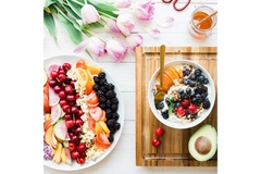 Healthy breakfast with a colorful fruit bowl, yogurt topped with berries and nuts, fresh avocado, and a vibrant fruit platter on a white table.